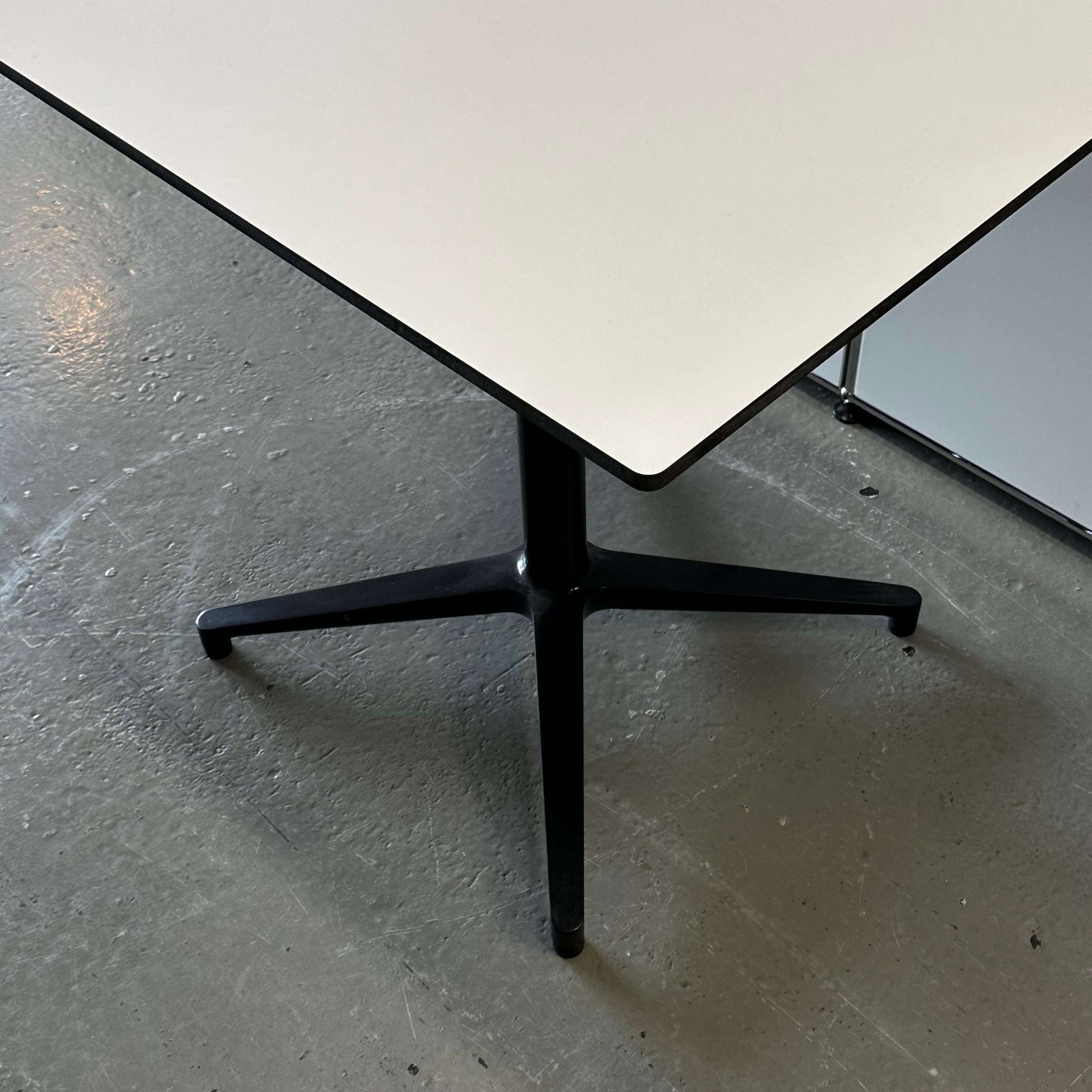 Vitra Bistro Table with white rectangular top and black metal pedestal base on concrete floor