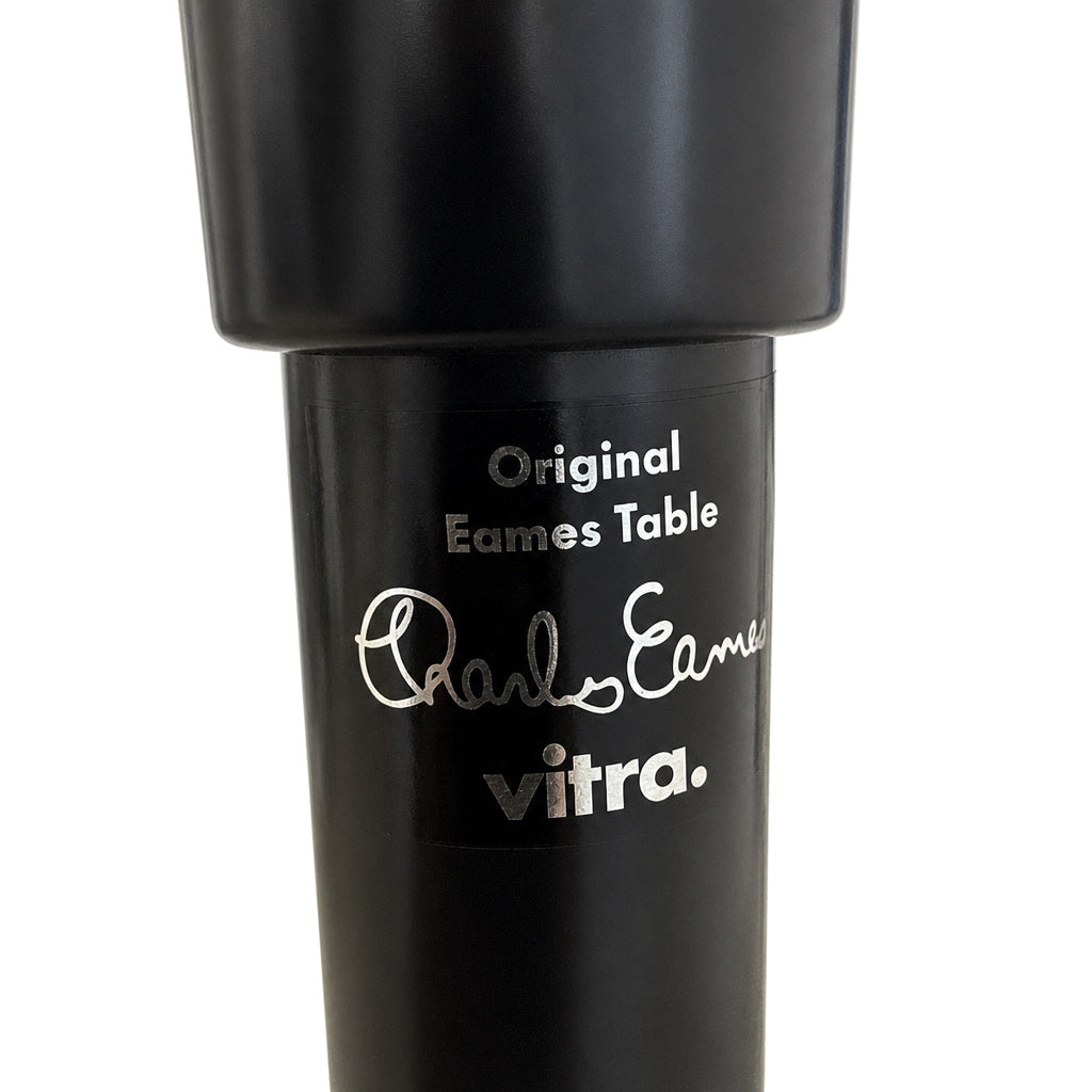 Schwarzes Vitra Contract Table Tischbein mit silbernem Eames-Logo und Signatur auf weißem Hintergrund.