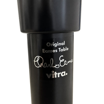 Schwarzes Vitra Contract Table Tischbein mit silbernem Eames-Logo und Signatur auf weißem Hintergrund.