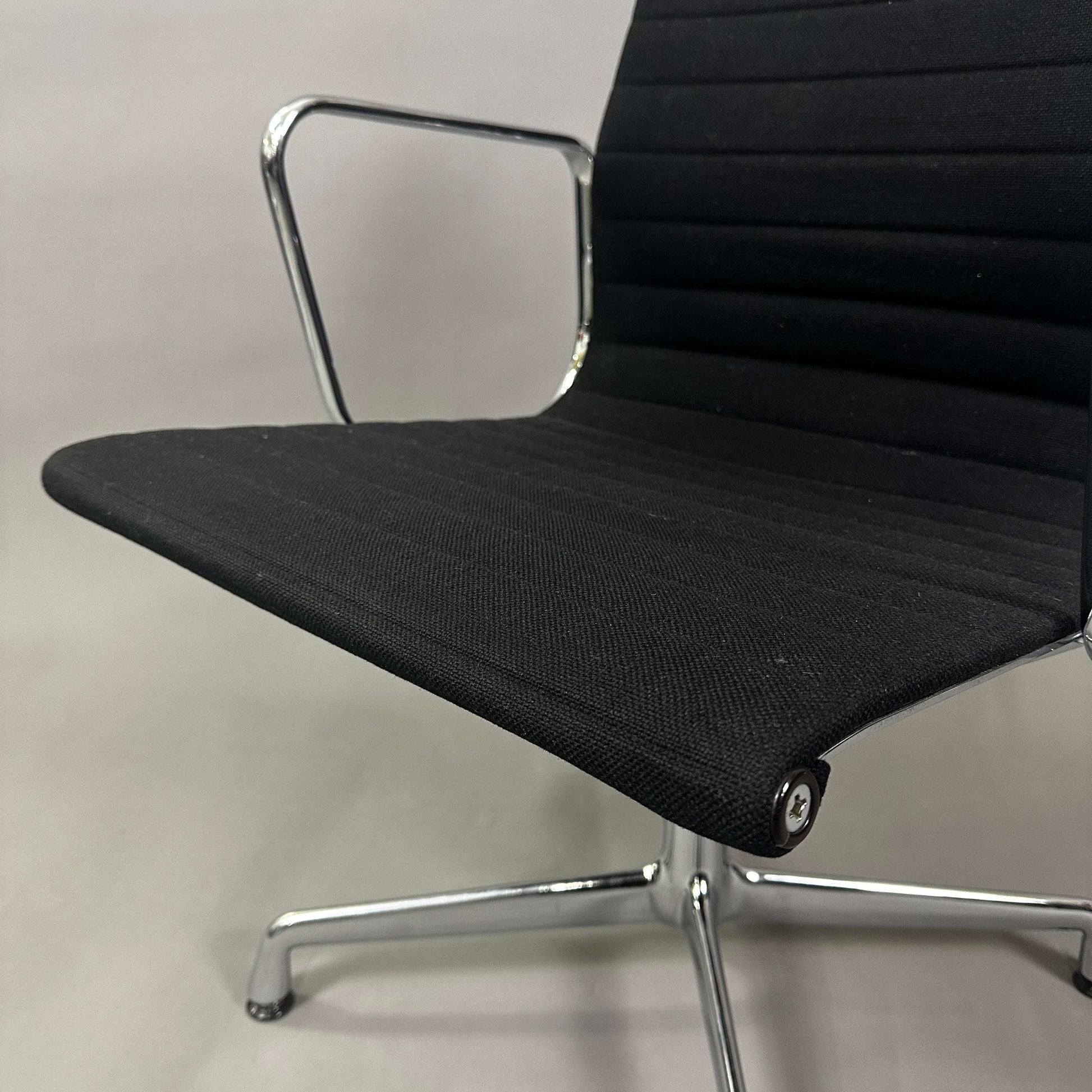 Close-up of a black Vitra EA 107 Hopsak non-swivel office chair with chromed aluminum frame and fabric upholstery.
