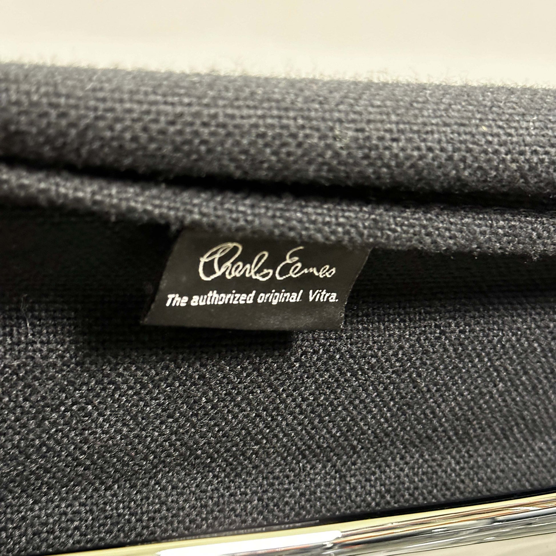 Close-up of black hopsak fabric and chrome frame on Vitra EA 108 Eames Alu Chair tag