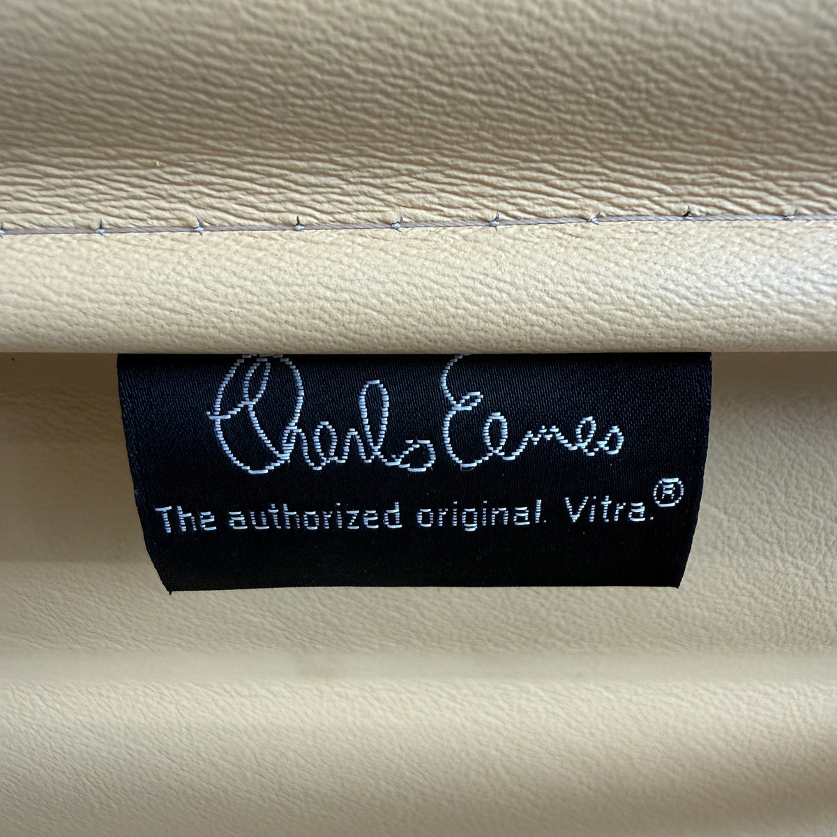Schwarzes Charles Eames Vitra-Label auf hochwertigem, cashewfarbenem Leder des Alu Chair EA 108.