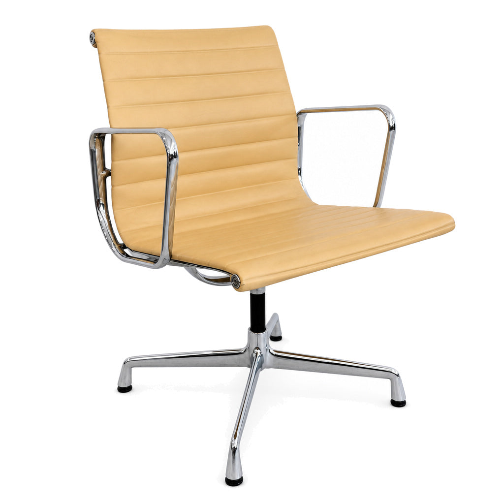 Vitra Eames Alu Chair EA108 in cashewfarbenem Leder mit verchromtem Gestell und Armlehnen vor weißem Hintergrund.