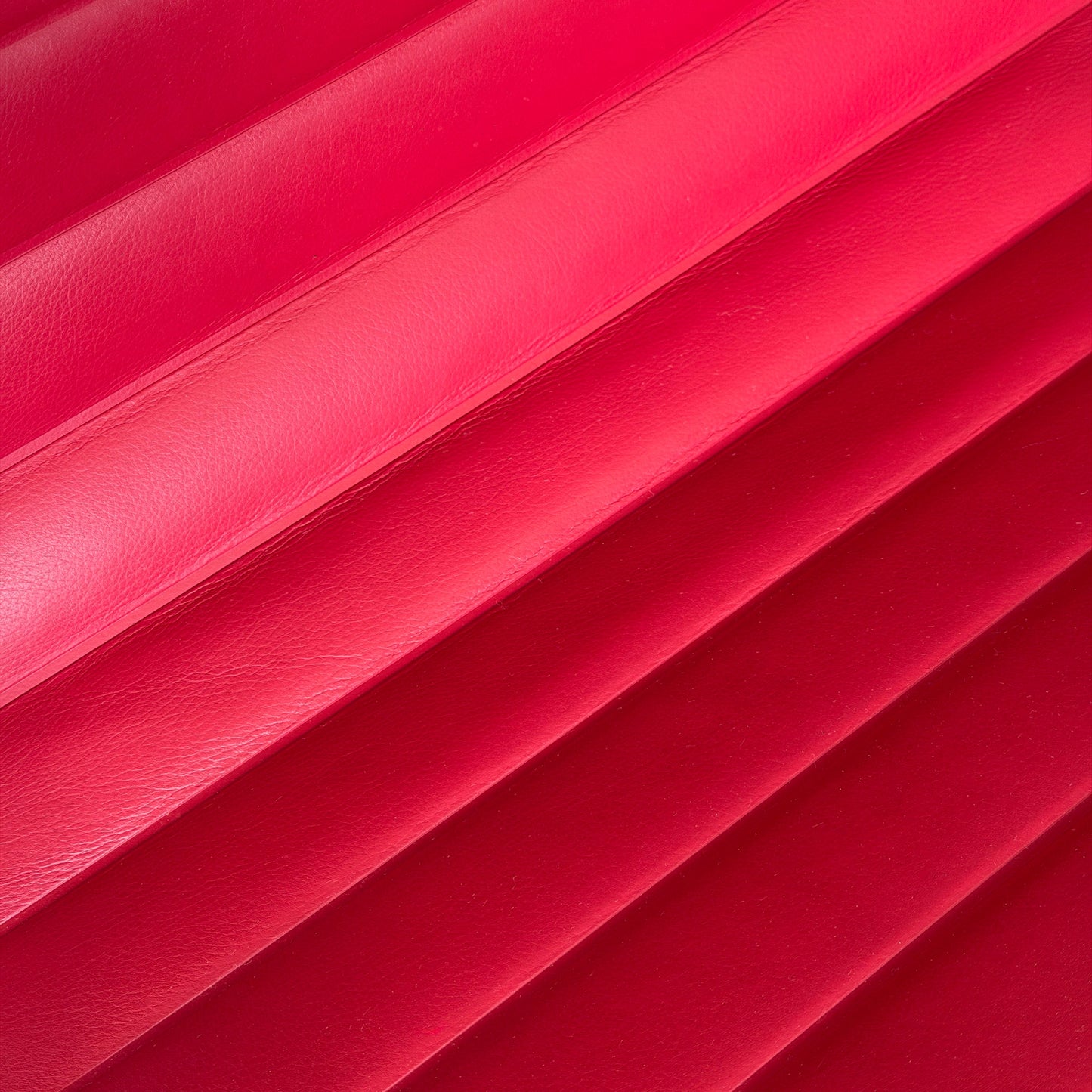 Nahaufnahme von rotem Leder mit horizontalen Falten, Vitra EA 108 Stuhlmaterial.