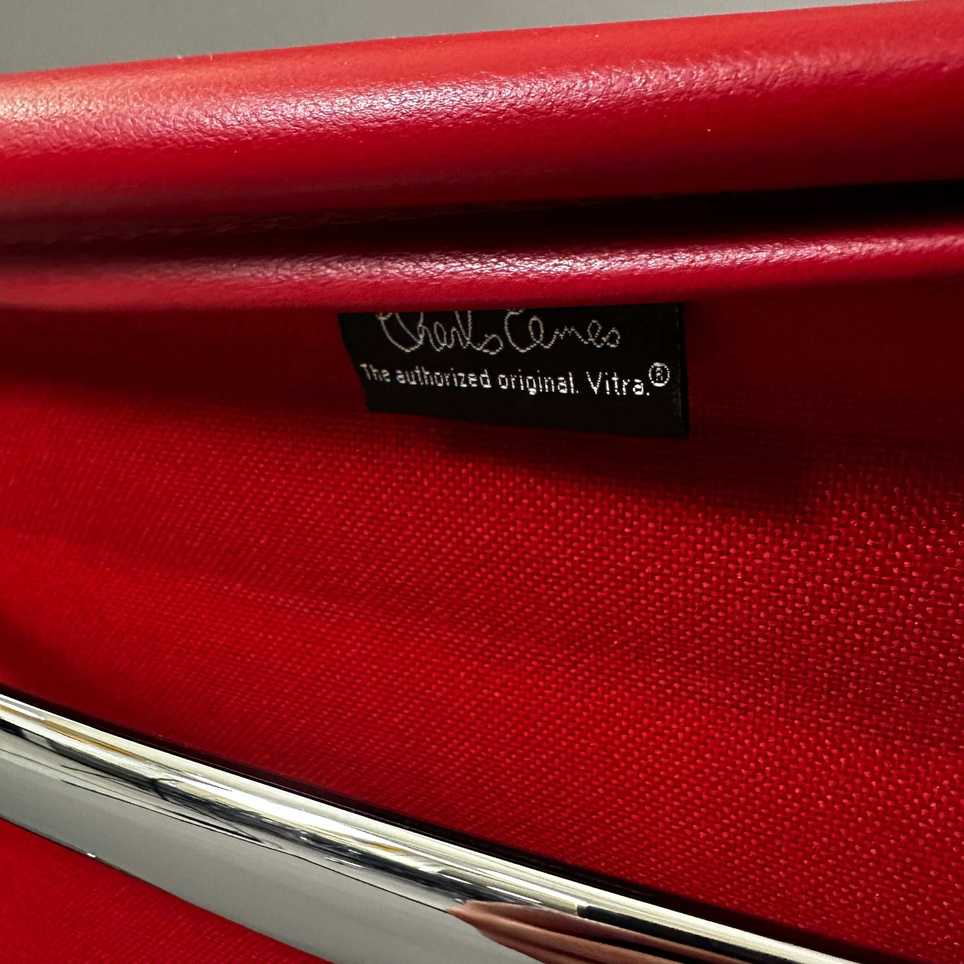 Close-up of red leather Vitra EA 108 swivel chair with chrome frame and Charles Eames label