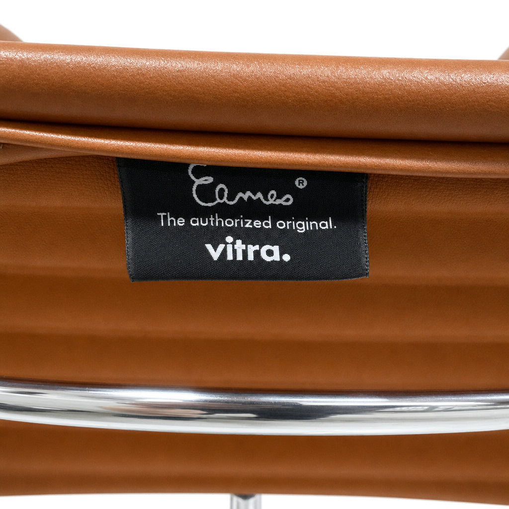 Vitra Eames EA 108 Stuhl mit cognacfarbenem Premium-Leder und poliertem Aluminiumrahmen inklusive Markenlabel.