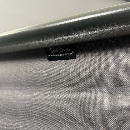 Nahaufnahme des grauen Lederbezugs und des polierten Aluminiumgestells des Vitra EA 112 Eames Alu Chair mit Vitra-Label