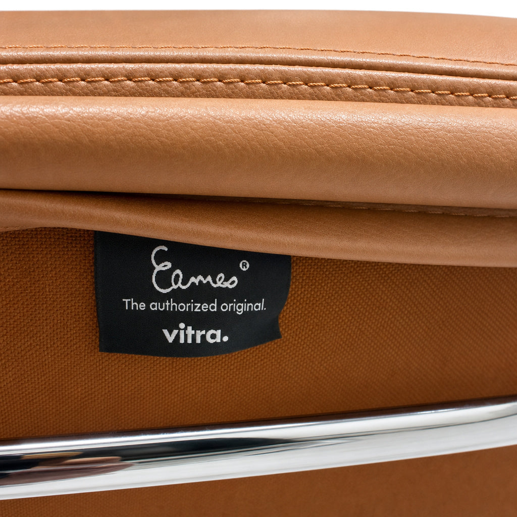 Detailaufnahme eines Vitra Eames EA 208 Stuhls mit cognacfarbenem Premium-Leder, Chromrahmen und Eames-Markenlabel.