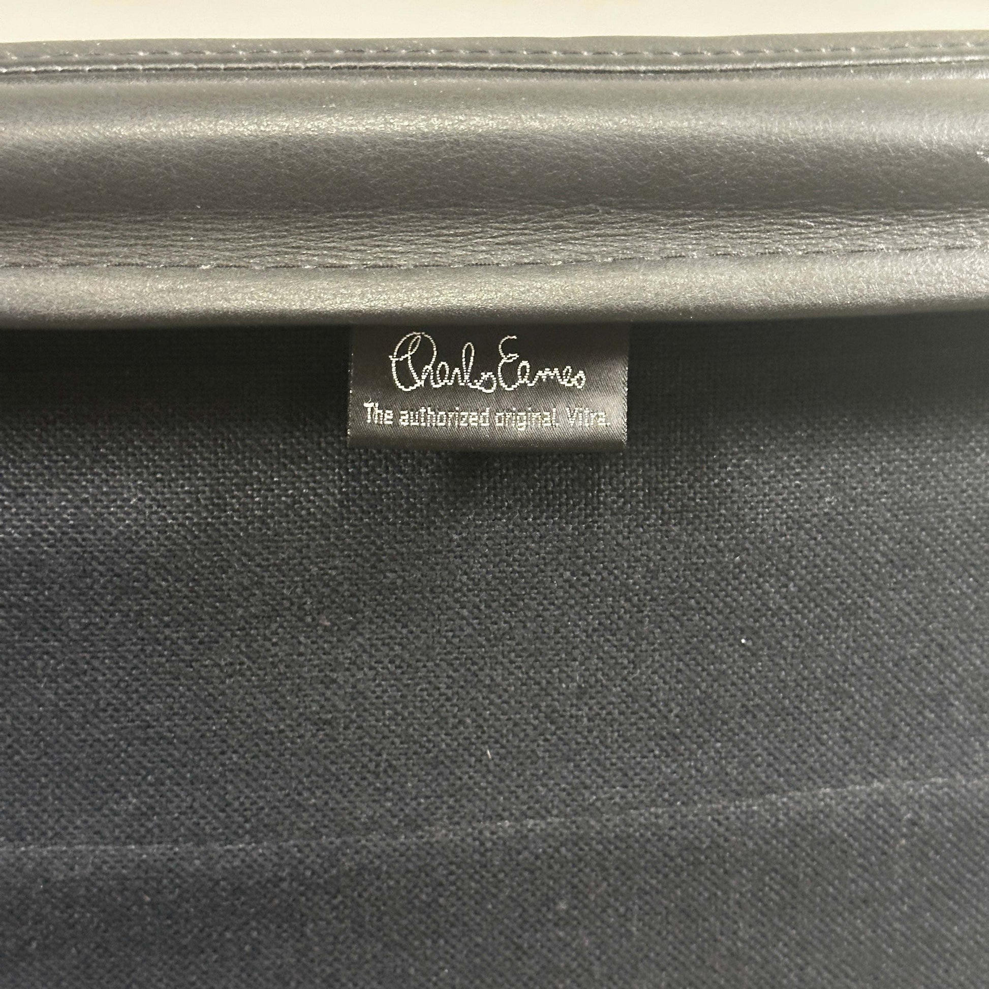 Close-up of black leather tag on Vitra EA 216 Eames Alu Chair soft pad upholstery