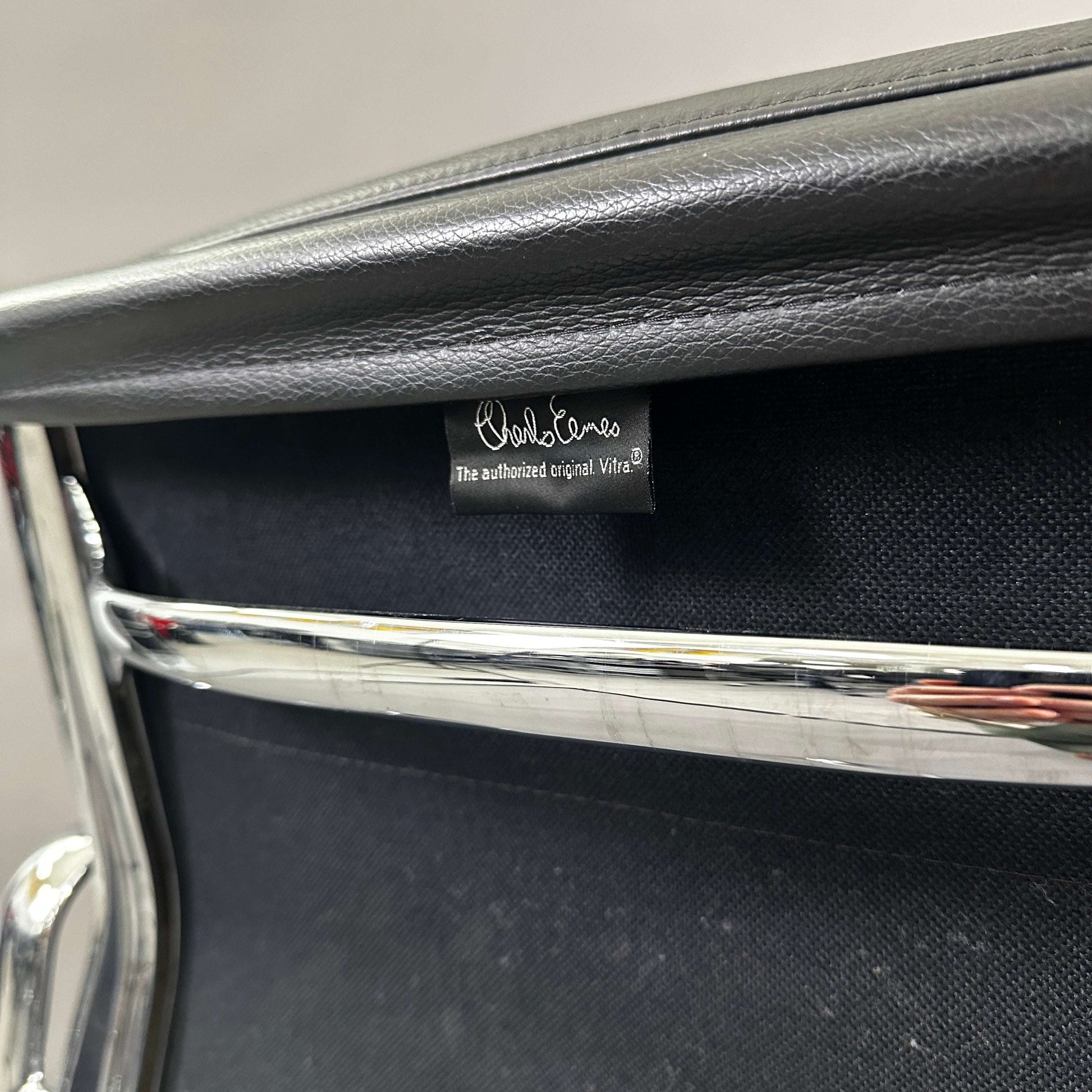 Close-up of Vitra EA 217 Eames Alu Chair with black leather upholstery and chrome frame showing authentic Vitra label