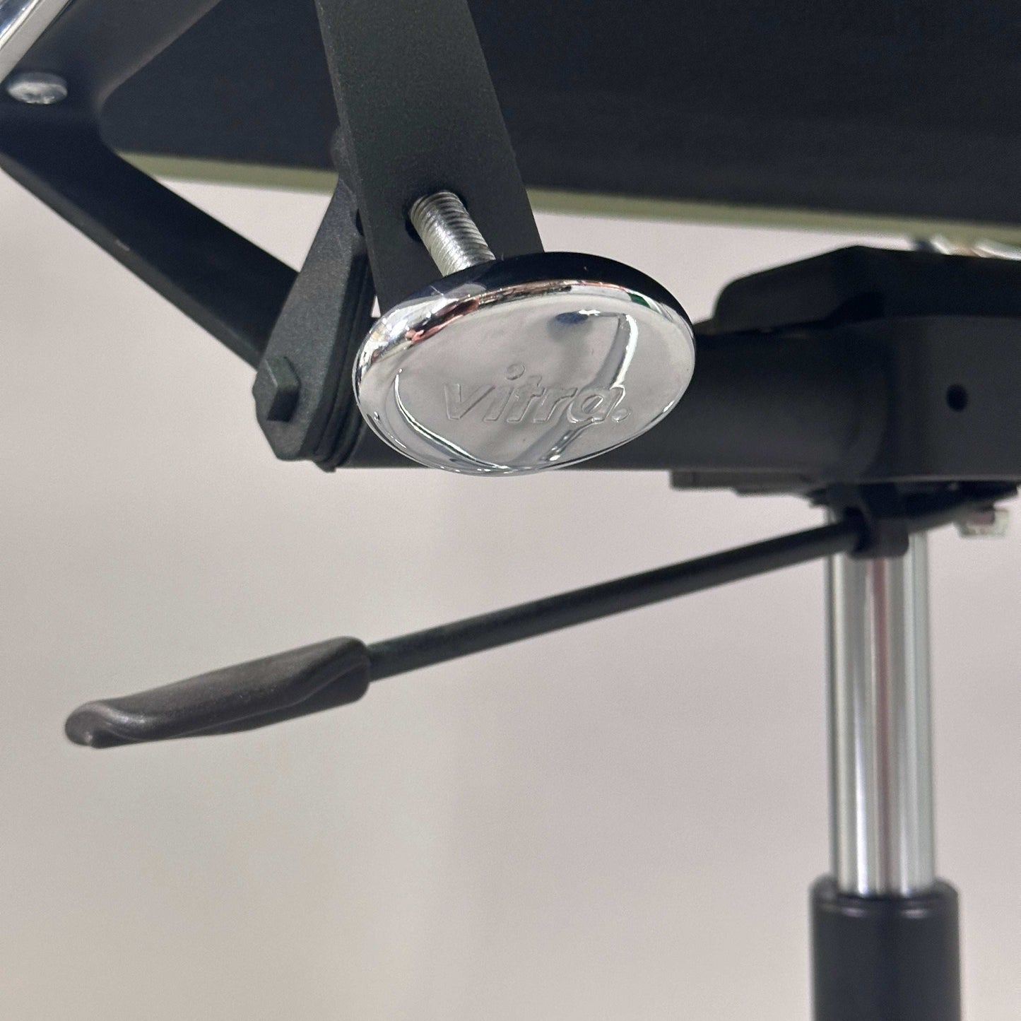 Detailaufnahme der verchromten Sitzhöhenverstellung des Vitra EA 219 Eames Alu Chair mit hellgrünem Lederbezug