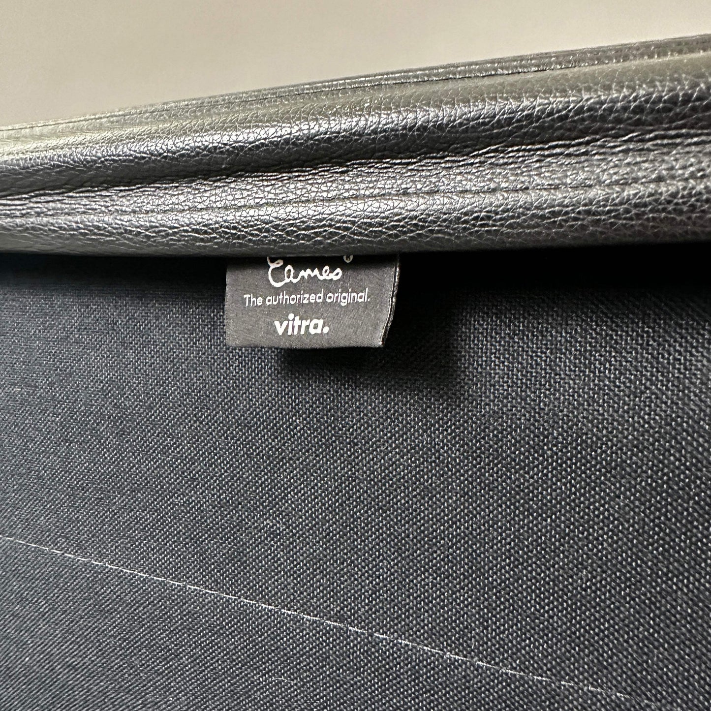 Detailaufnahme des schwarzen Lederbezugs und Vitra Eames EA 219 Labels am polierten Aluminiumstuhl