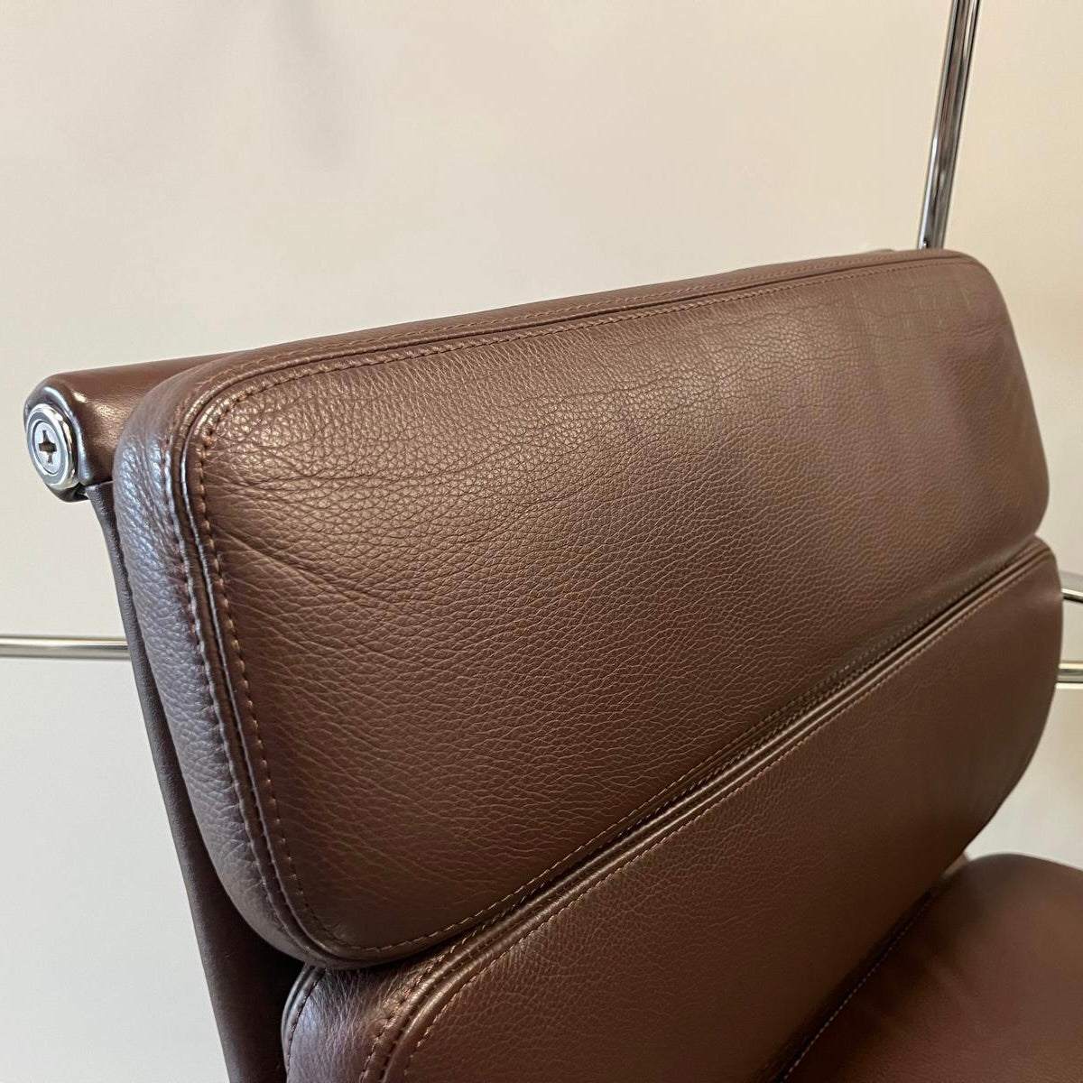 Close-up of chestnut brown leather padded backrest of Vitra EA Soft Pad Chair with chrome frame