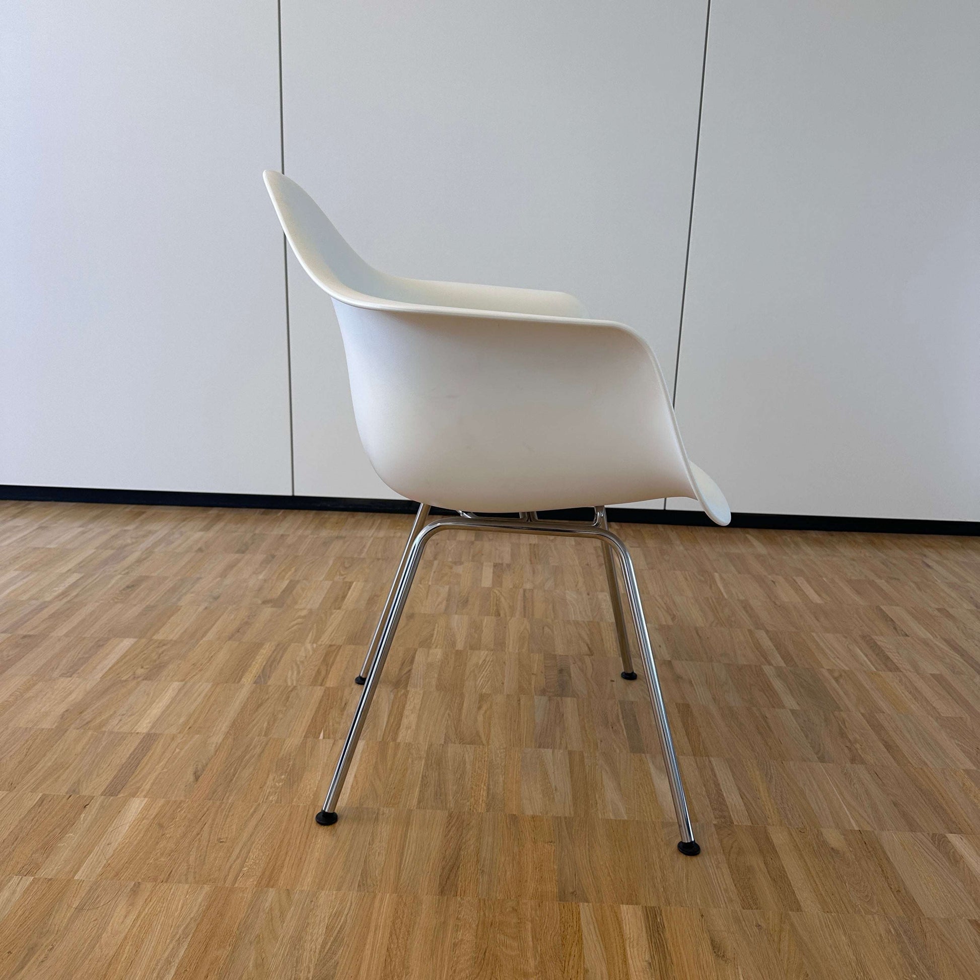 Vitra Eames Plastic Armchair weiß mit verchromtem Metallgestell auf Holzfußboden vor weißer Wand