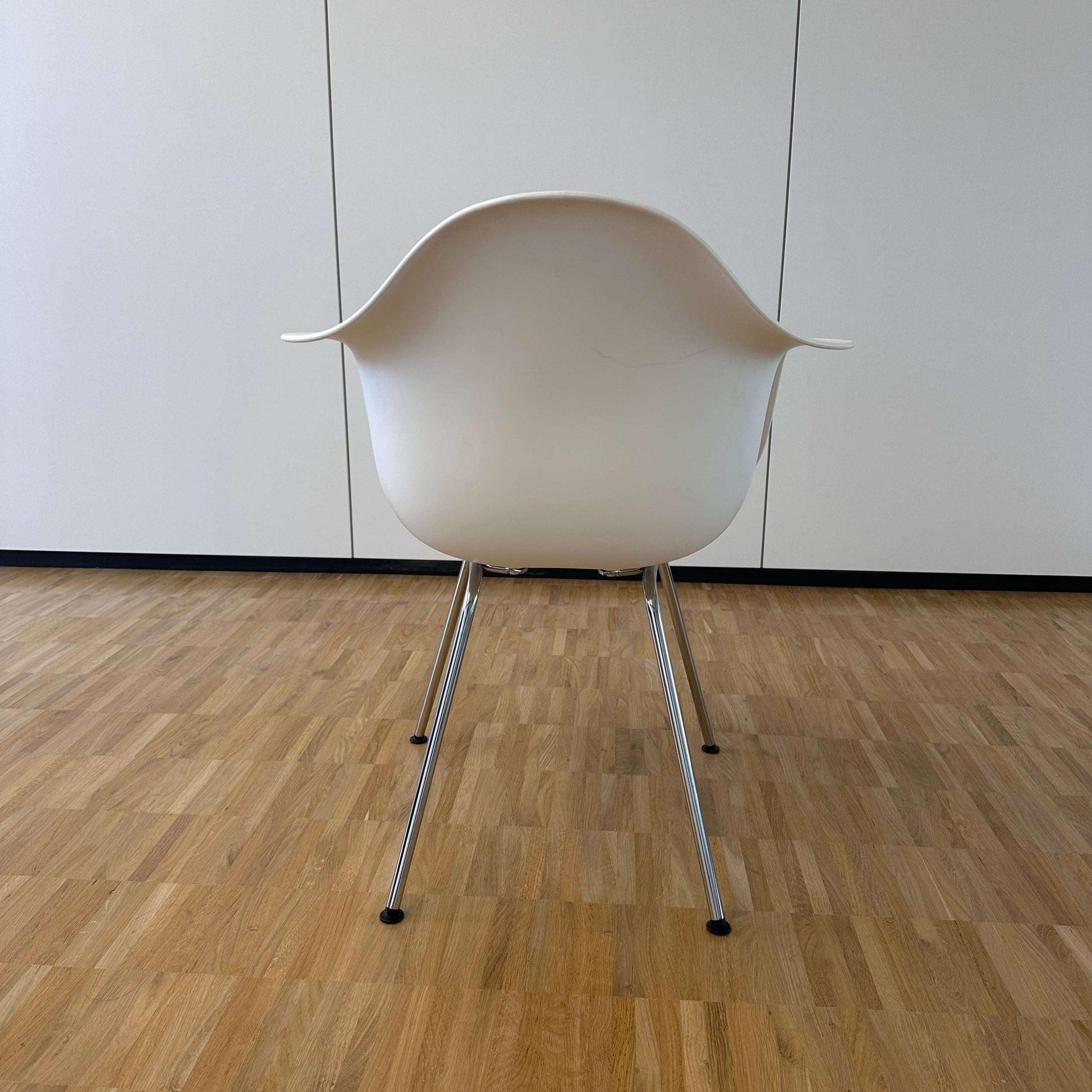 Vitra Eames Plastic Armchair weiß mit verchromtem Metallgestell und ergonomischer Sitzschale aus weißem PE, Rückansicht auf Parkettboden