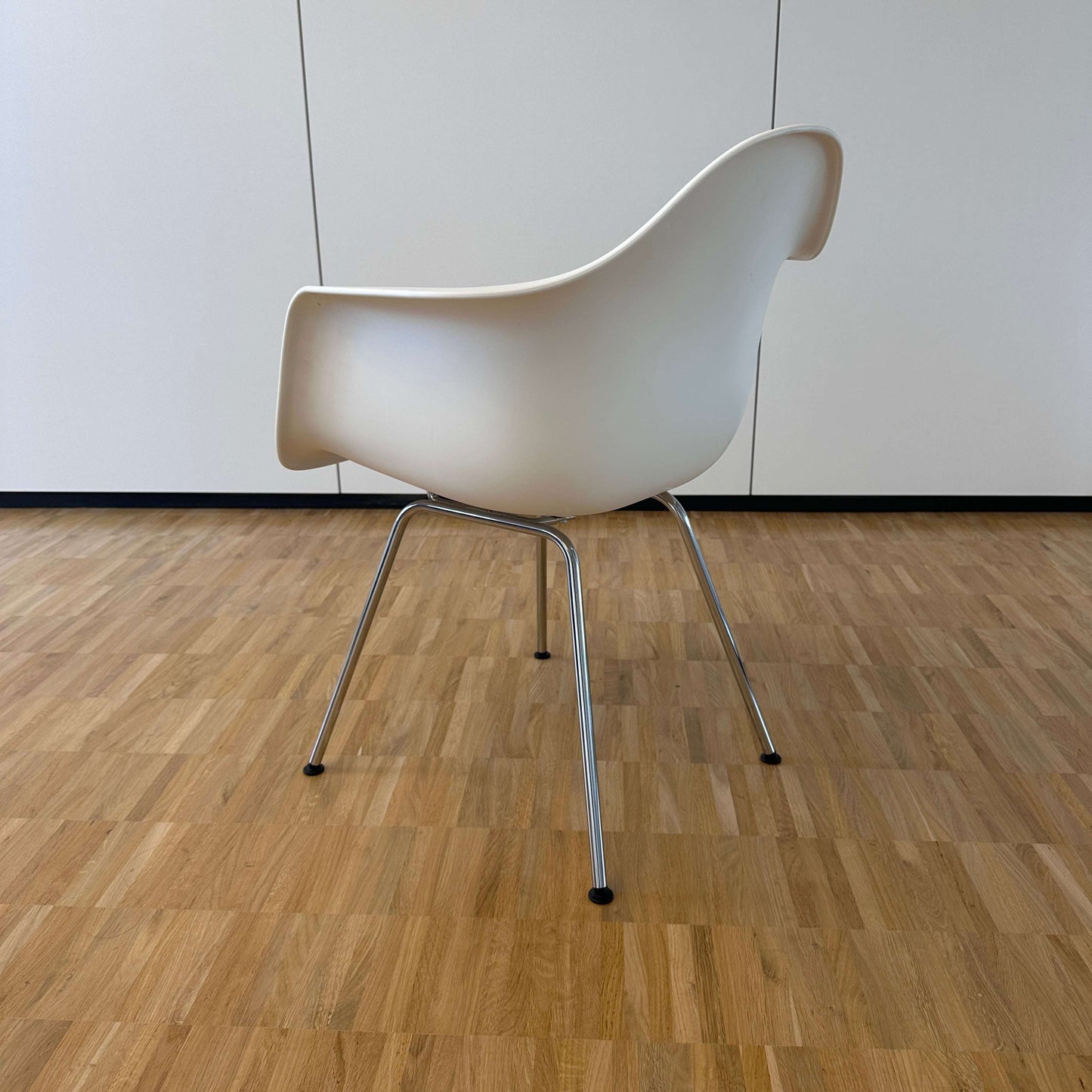 Vitra Eames Plastic Armchair weiß mit verchromtem Metallgestell auf Parkettboden, Rückansicht