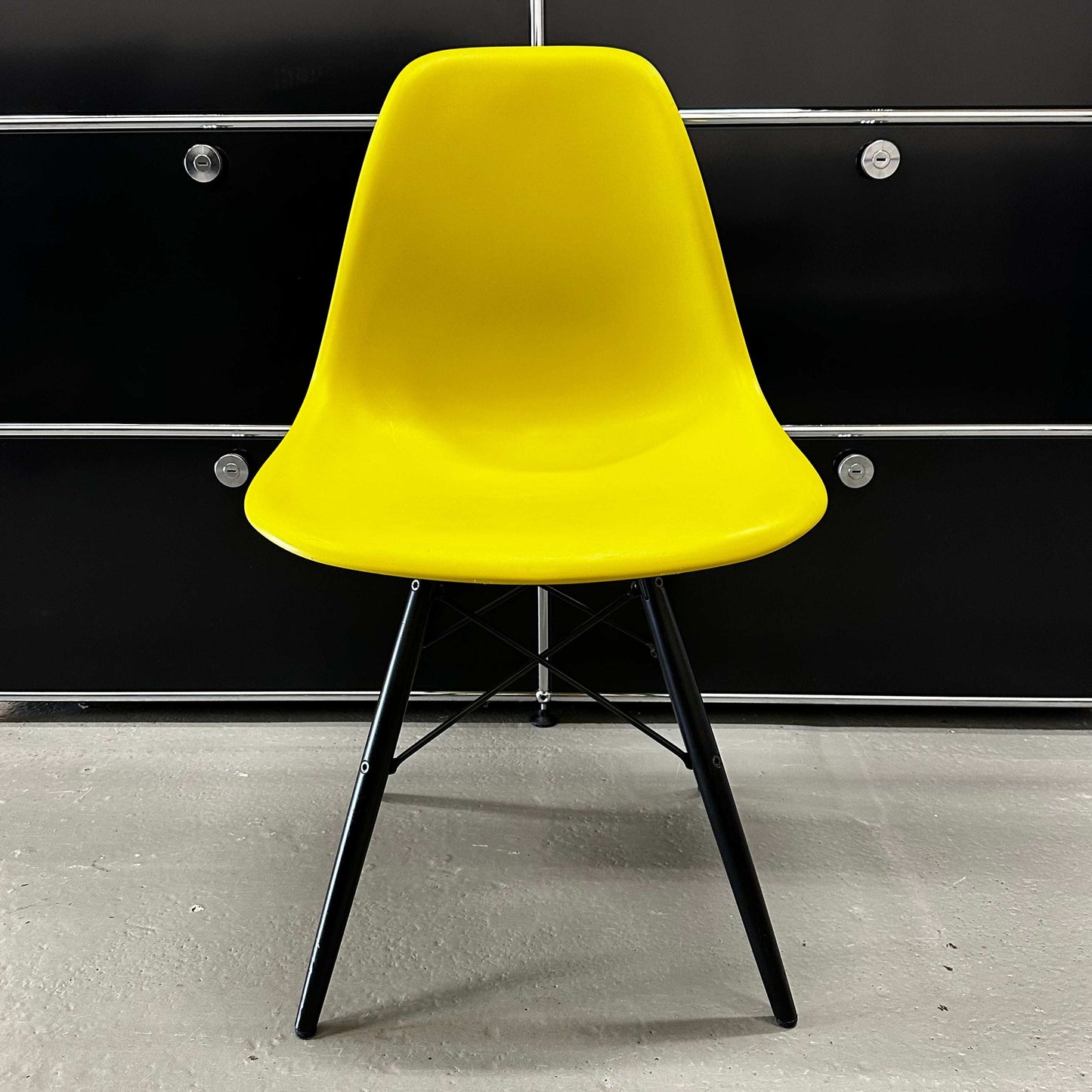 Vitra Eames Plastic Sidechair with mustard yellow seat and black wooden legs against black cabinet background