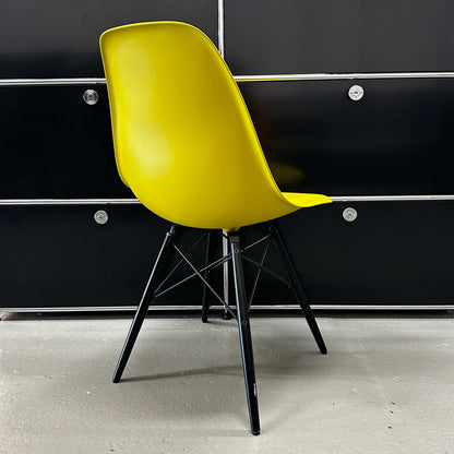 Vitra Eames Plastic Sidechair with mustard plastic seat and black wooden legs against black background