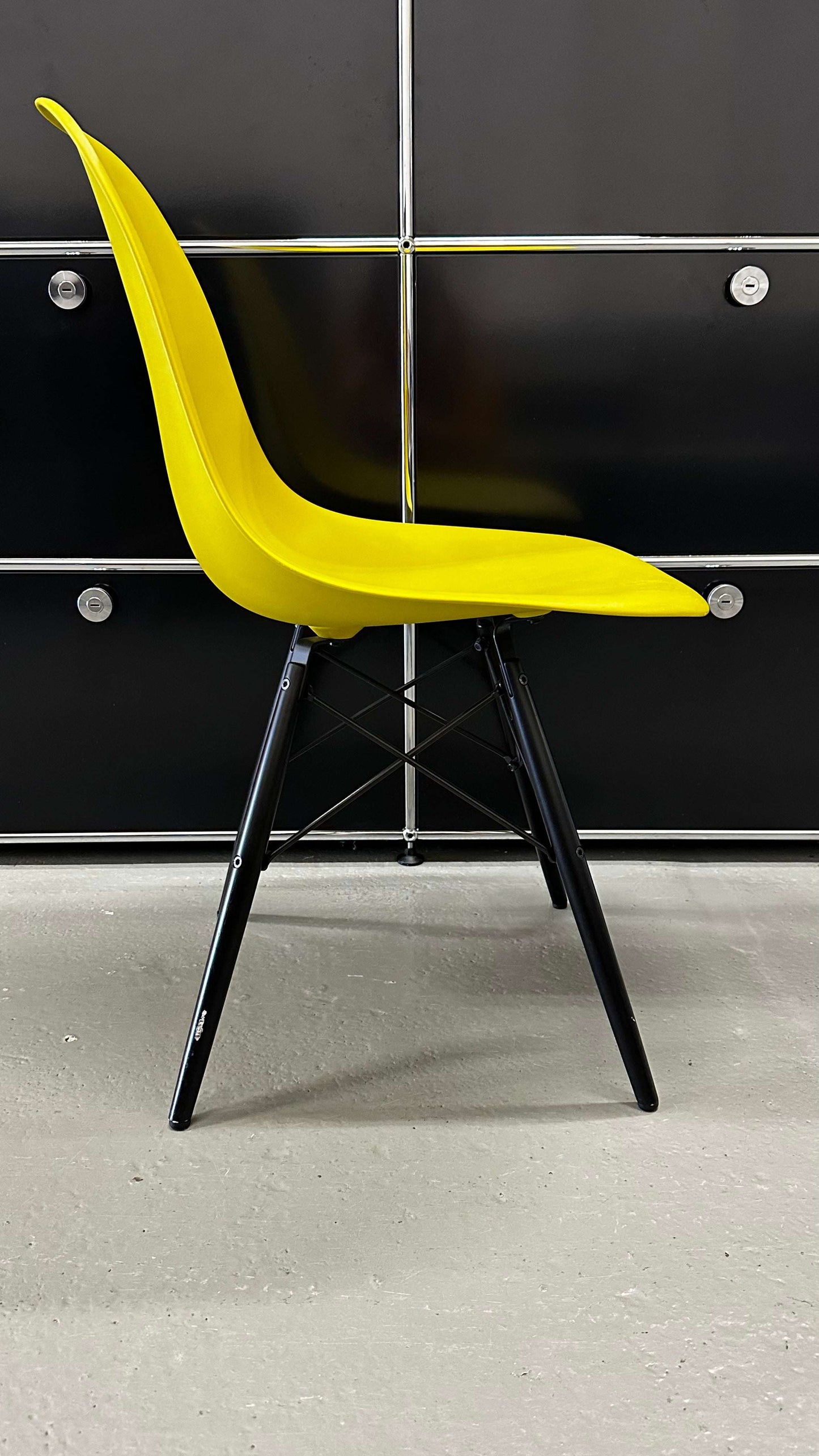 Vitra Eames Plastic Sidechair with mustard yellow seat and black wooden legs against black panel background