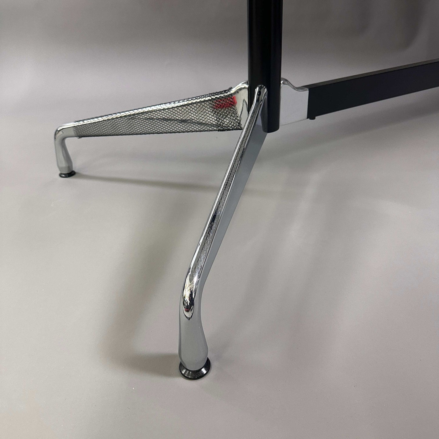 Detailaufnahme des Chromfußes des Vitra Eames Segmented Table mit weißer HPL-Tischplatte und schwarzer Kante