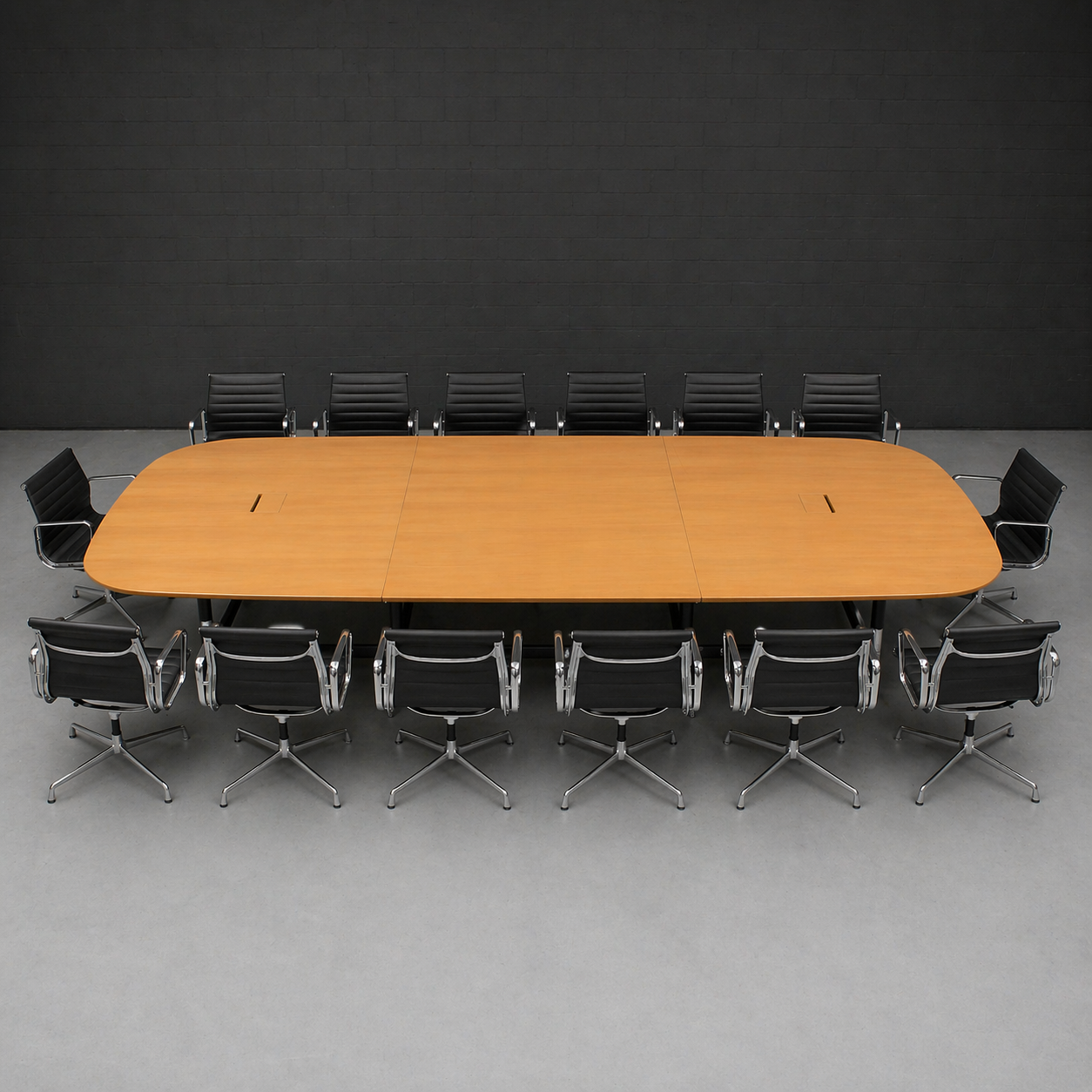 Vitra Eames Segmented Table, 430x250cm, Eichenfurnier, mit zwei Elektrifizierungen, umgeben von schwarzen Lederstühlen.