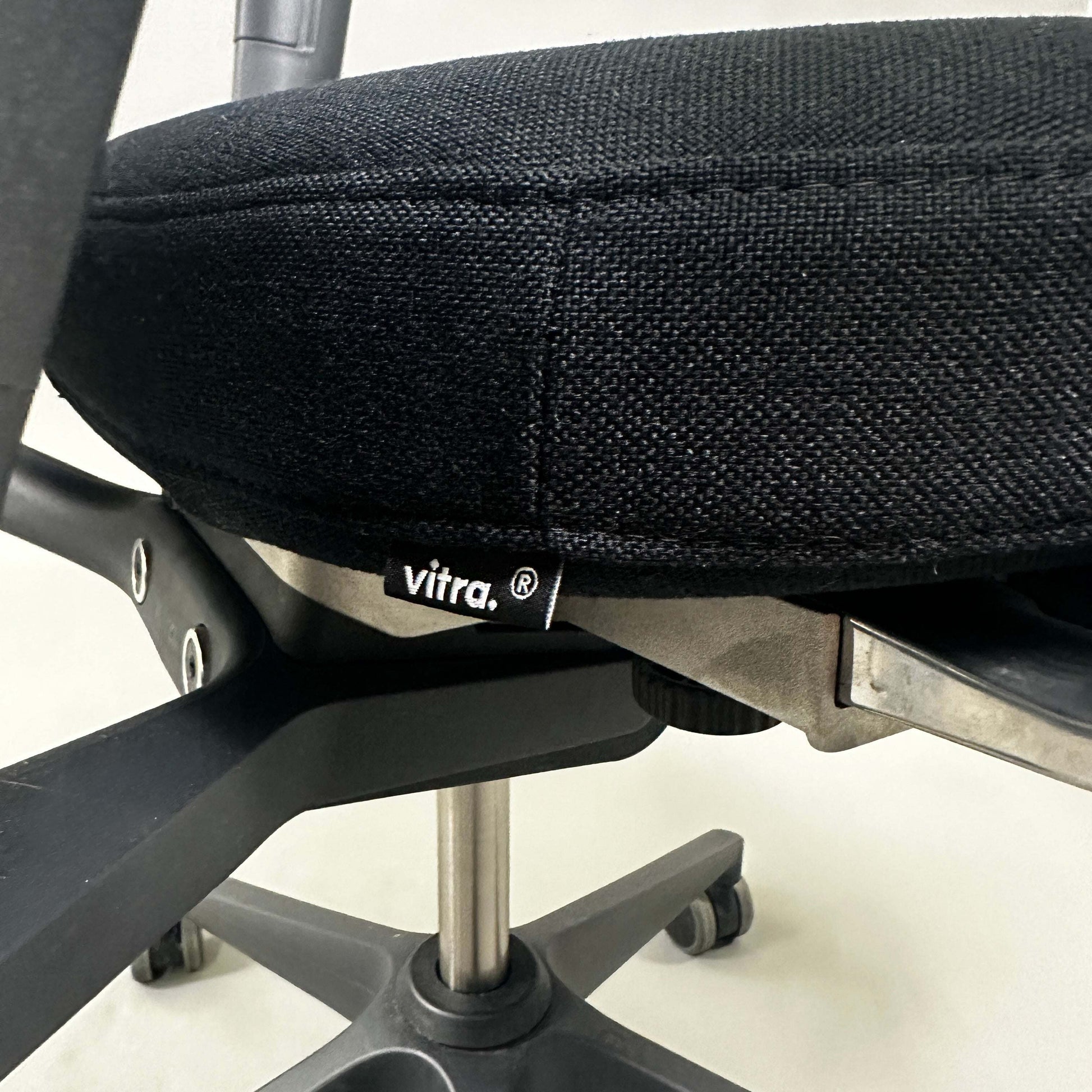 Close-up of black Vitra ID Mesh office chair seat and adjustable height mechanism with black plastic frame and caster wheels.