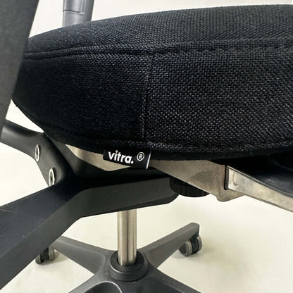 Close-up of black Vitra ID Mesh office chair seat and adjustable height mechanism with black plastic frame and caster wheels.
