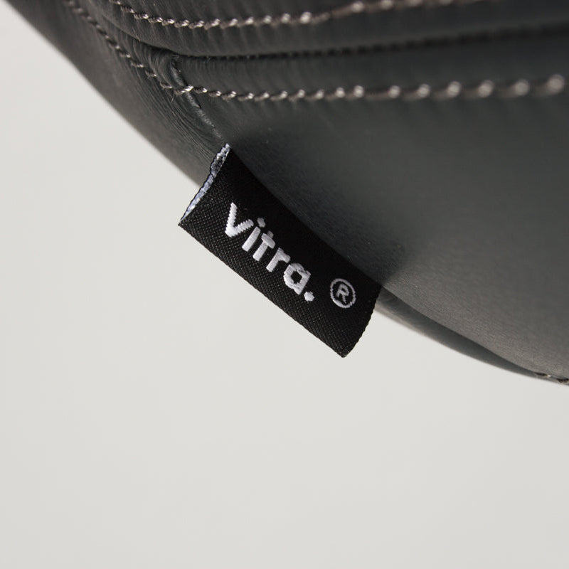 Vitra Petit Repos Sessel aus umbragrauem Premiumleder mit weißer Naht und Vitra-Label.