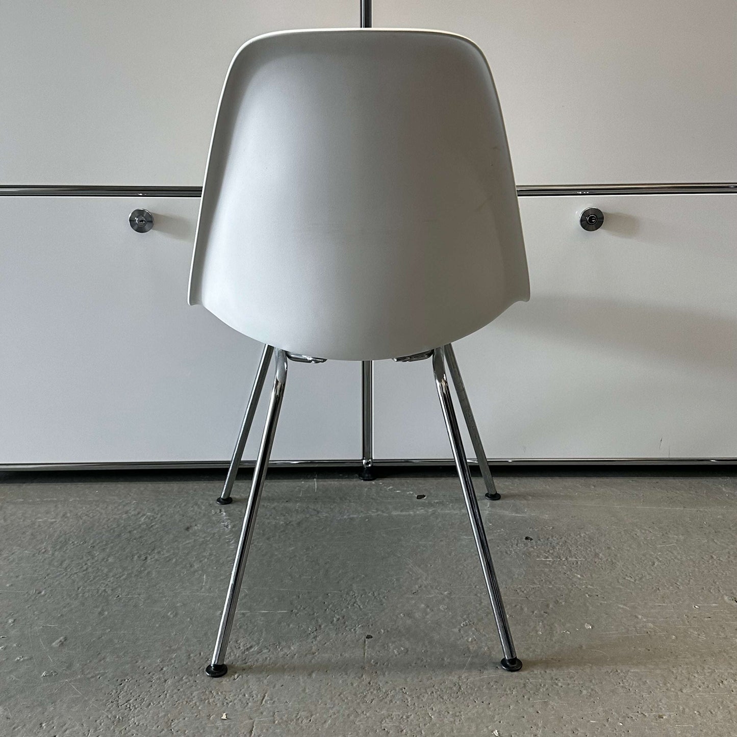 Vitra Plastic Side Chair in white plastic with metal legs shown from the back on a concrete floor