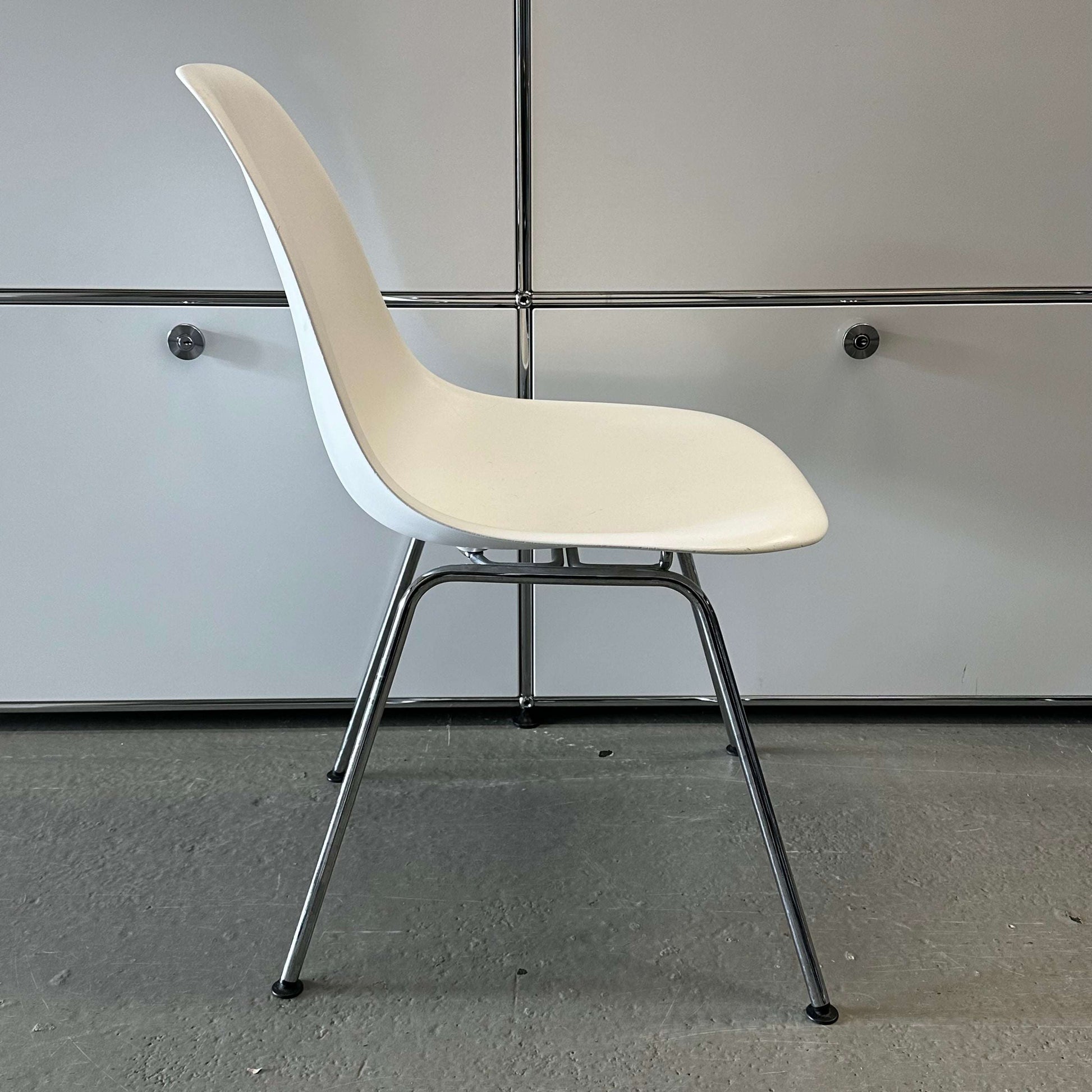 White Vitra Plastic Side Chair with chrome metal legs and minimalist design against gray background