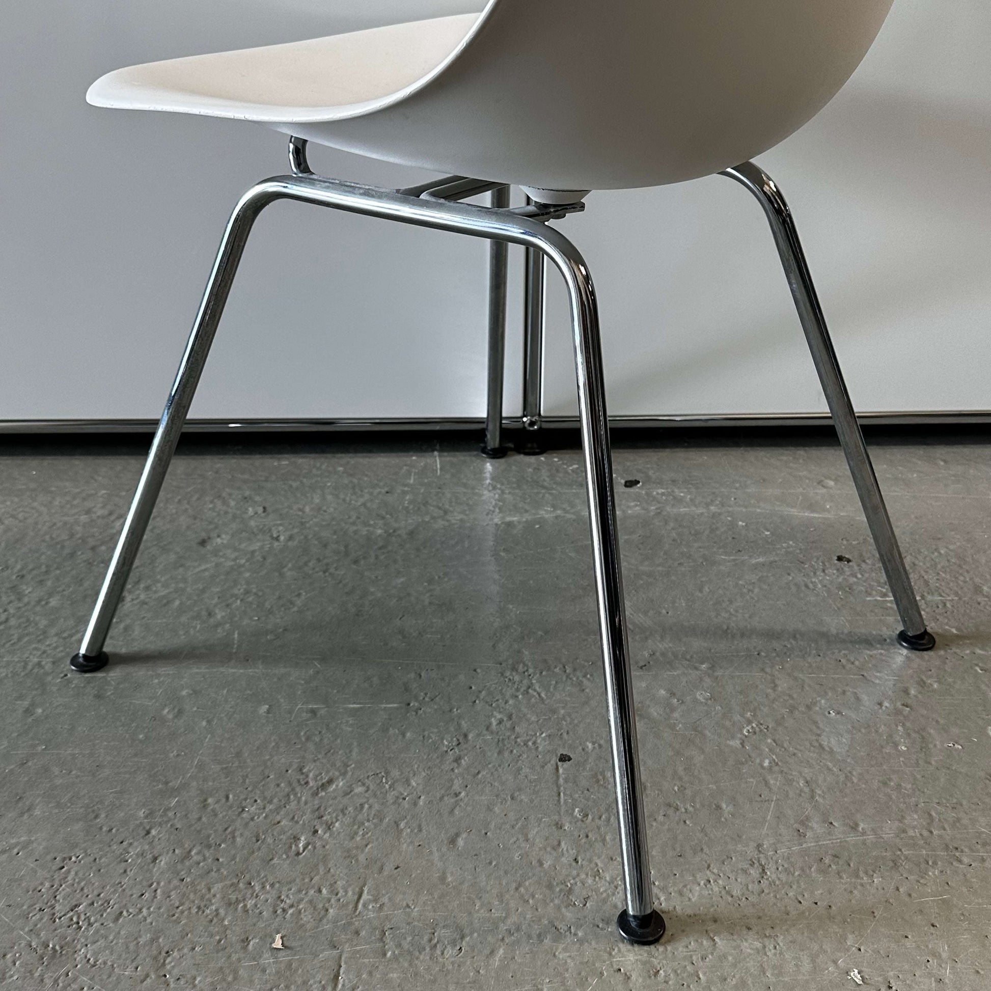 White Vitra Plastic Side Chair with chrome metal legs on a gray floor