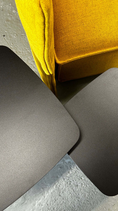 Close-up of yellow Vitra Plume Fauteuil armchair with two gray table surfaces