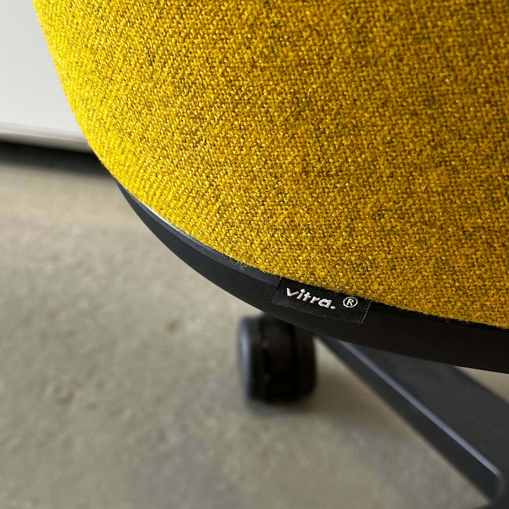 Close-up of yellow Vitra Softshell Drehstuhl fabric and five-star black swivel base with caster wheels