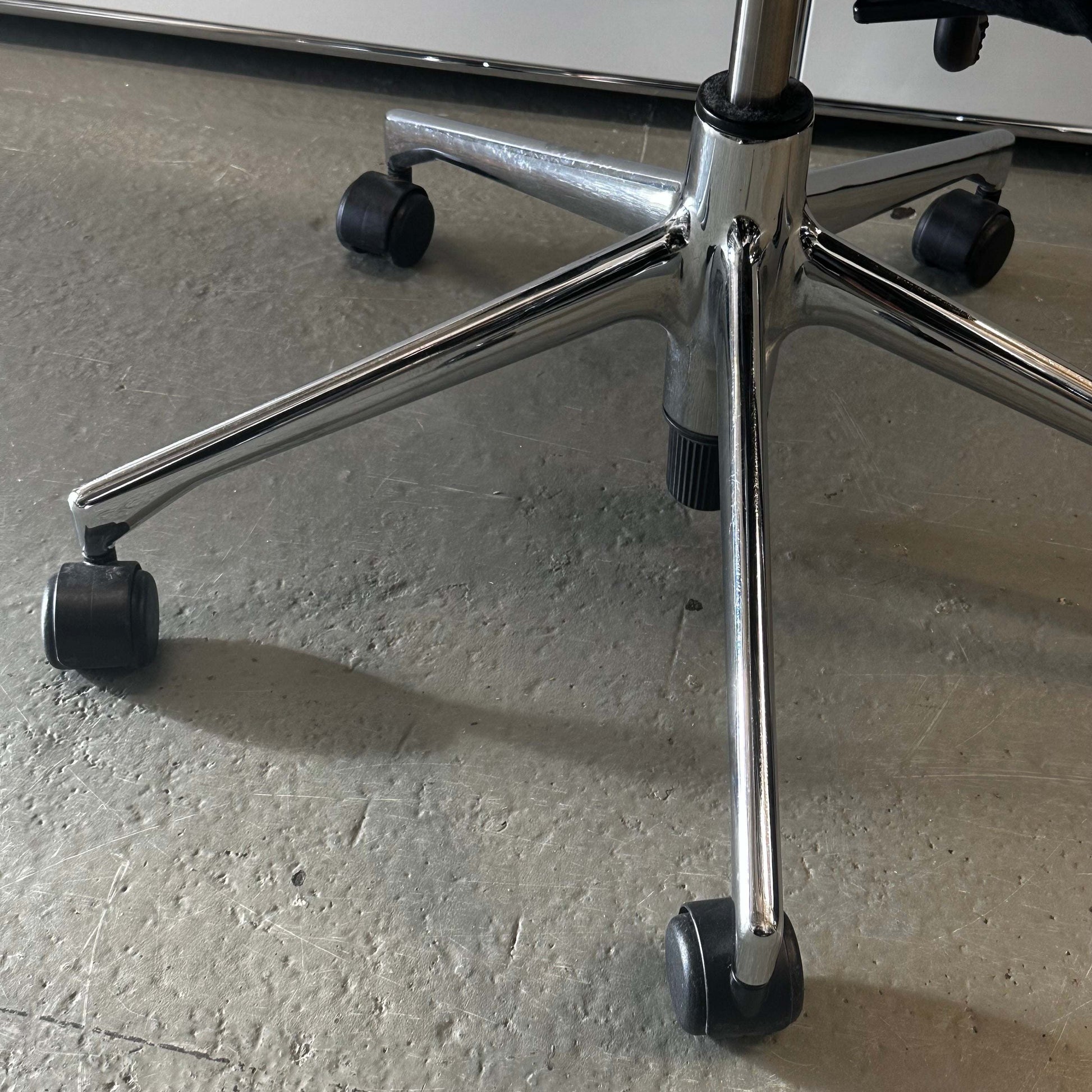 close-up of chrome base and wheels of a Vitra T-Chair Schwarz office chair on textured floor