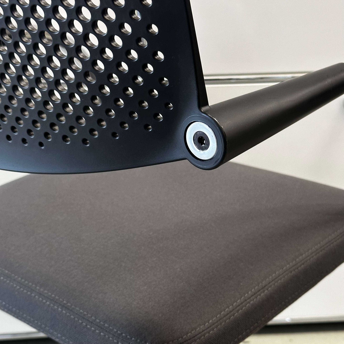 Close-up of Vitra Visavis 2 chair with dark grey fabric seat, black plastic perforated backrest, and chrome frame