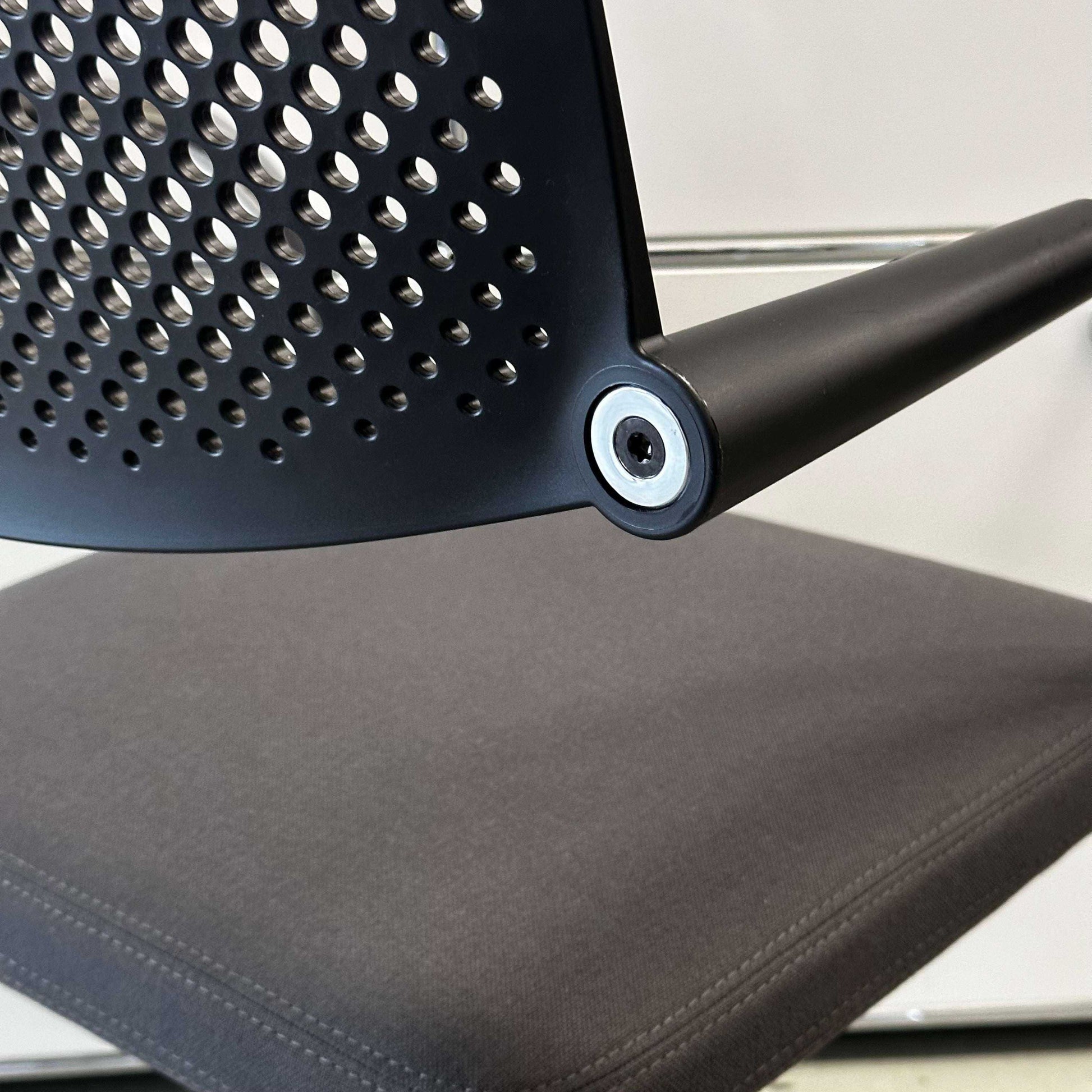 Close-up of Vitra Visavis 2 chair with dark grey fabric seat, black plastic perforated backrest, and chrome frame