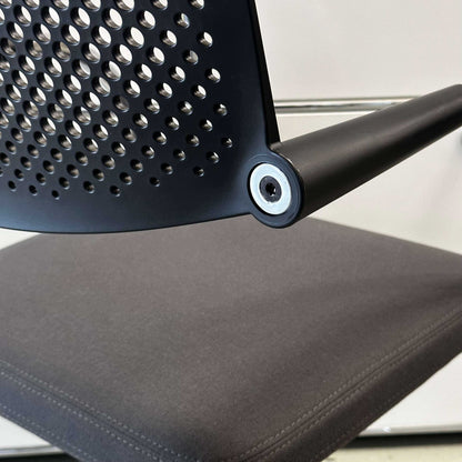 Close-up of Vitra Visavis 2 chair with dark grey fabric seat, black plastic perforated backrest, and chrome frame