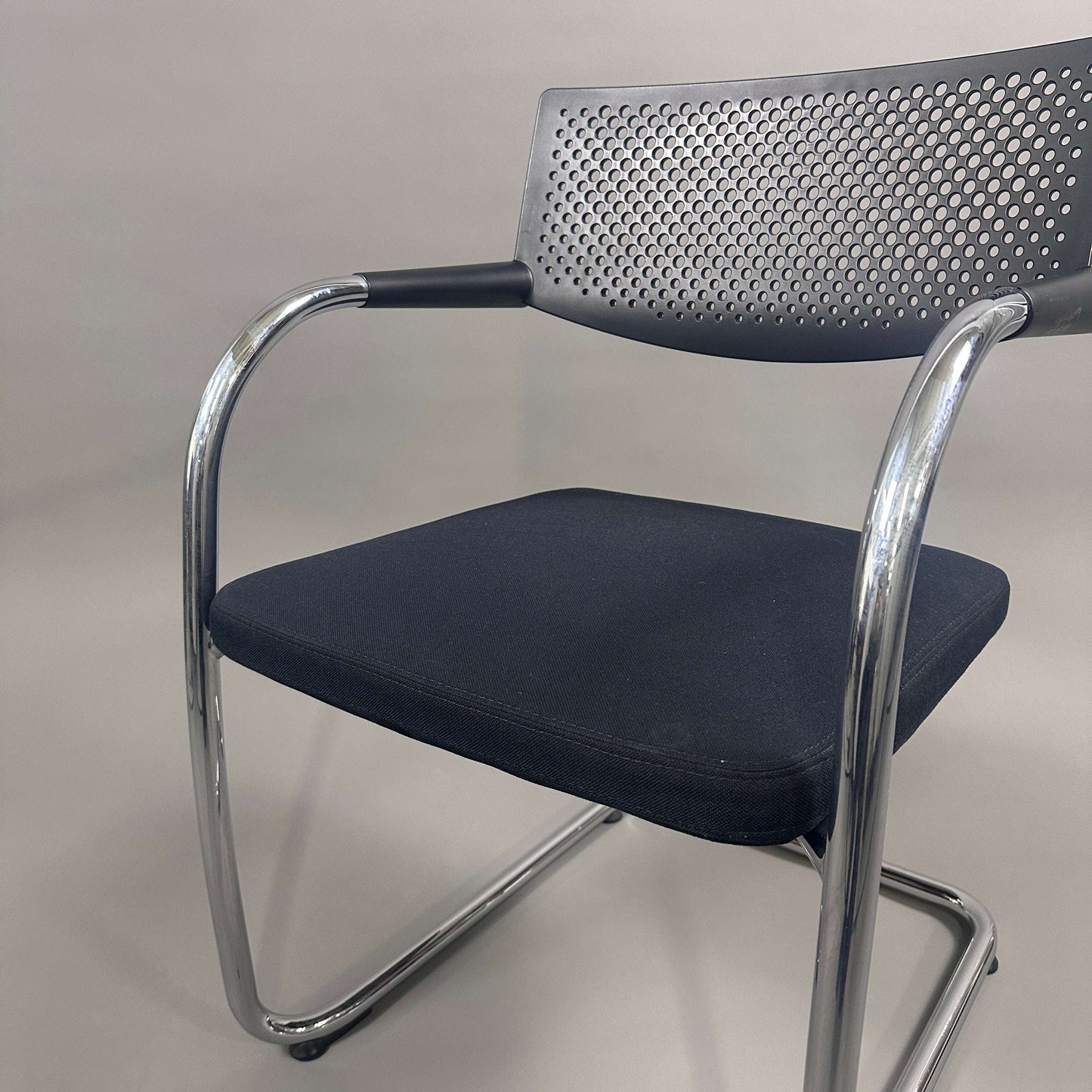 Black Vitra Visavis 2 visitor chair with fabric seat, perforated black plastic backrest, and chrome frame