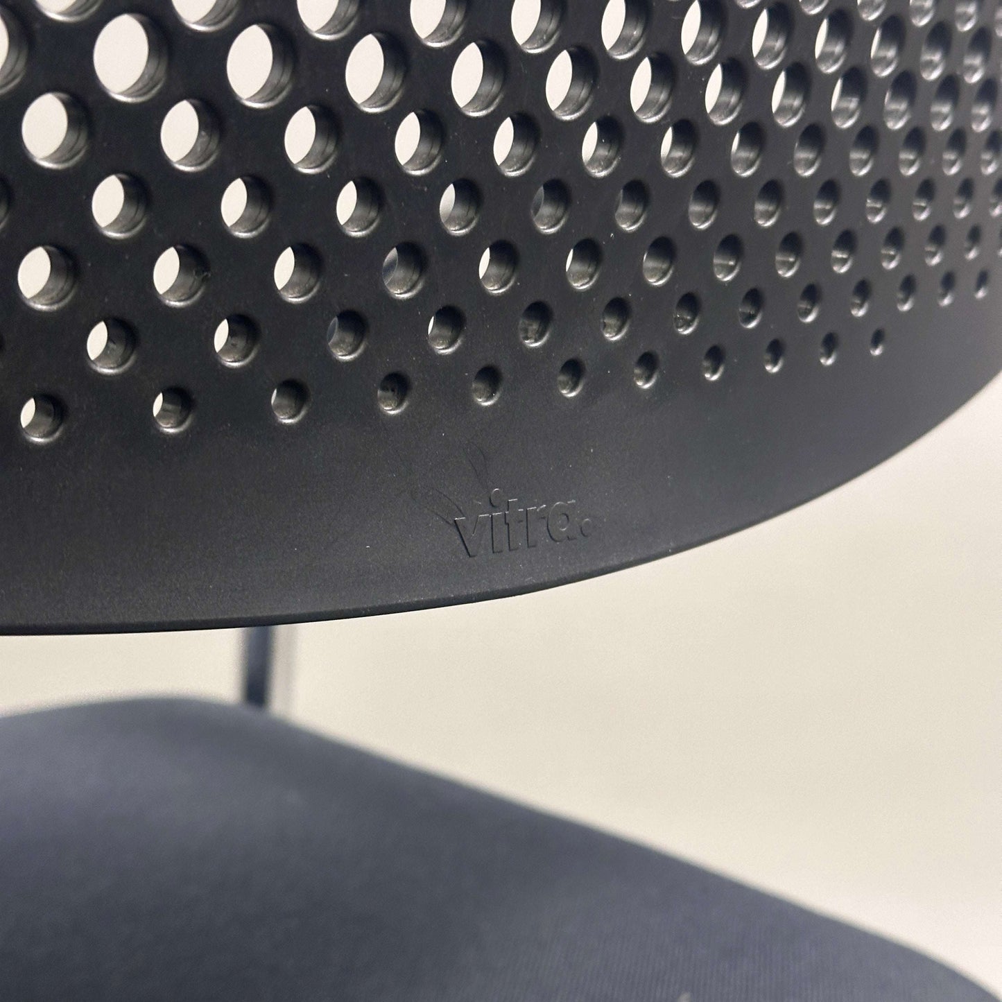 Close-up of black Vitra Visavis 2 chair with perforated plastic backrest and fabric seat