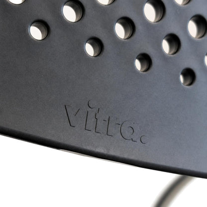 Vitra Visavis 2 Stuhl mit gelochter grauer Kunststoff-Rückenlehne und eingeprägtem Vitra-Logo.