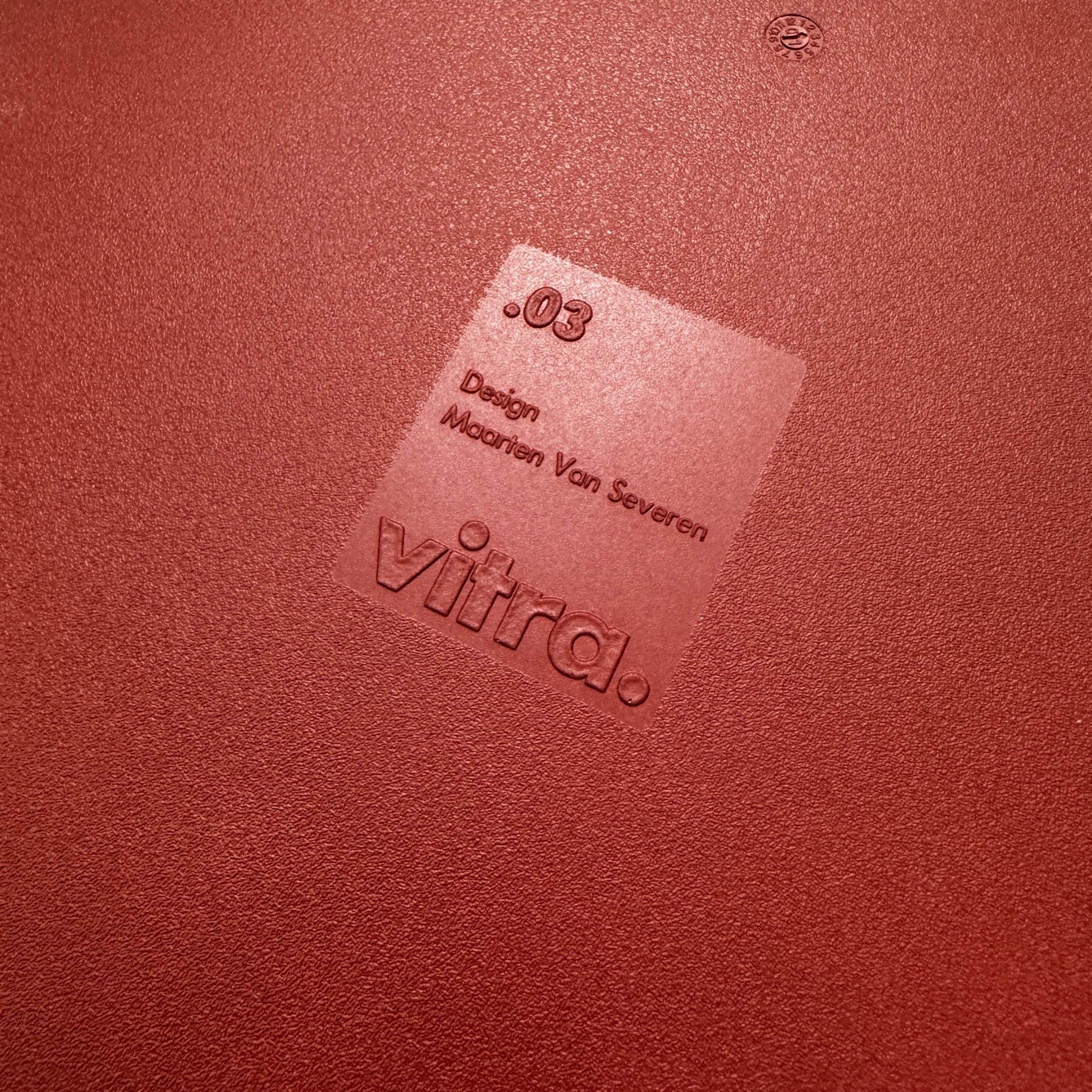 Close-up of red Vitra .03 Besucherstuhl seat with embossed logo and designer name Maarten Van Severen